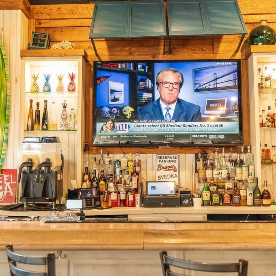A restaurant bar with a green surfboard, liquor bottles, and a TV displaying sports news.