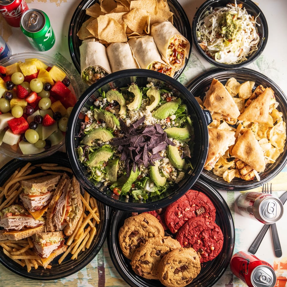 Catering spread with wraps, salad, sandwiches, fruit, and cookies.