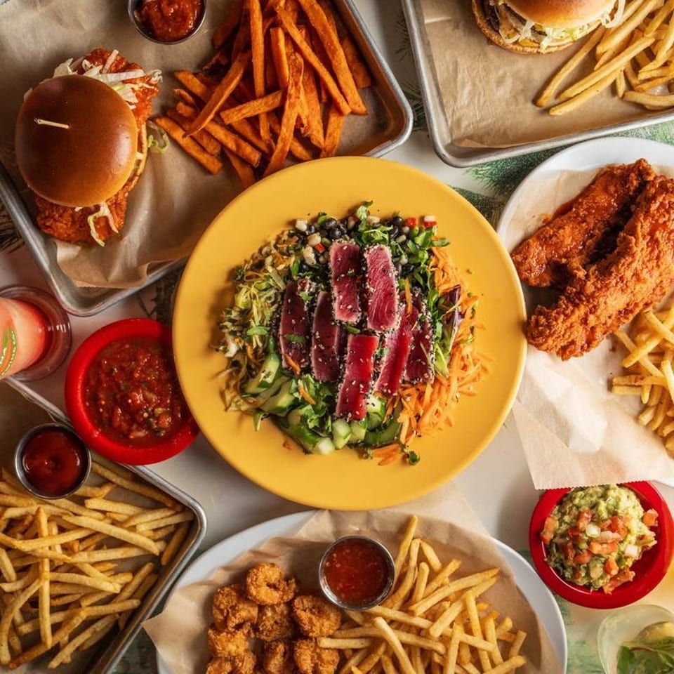 Overhead view of a table laden with various dishes including tuna salad, burgers, fries, and fried shrimp.