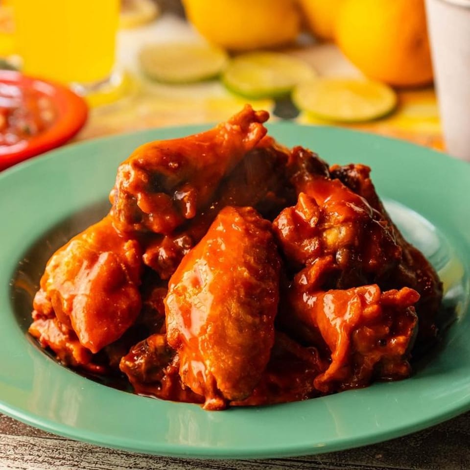 Spicy buffalo chicken wings on a green plate, with drinks and limes in the background.