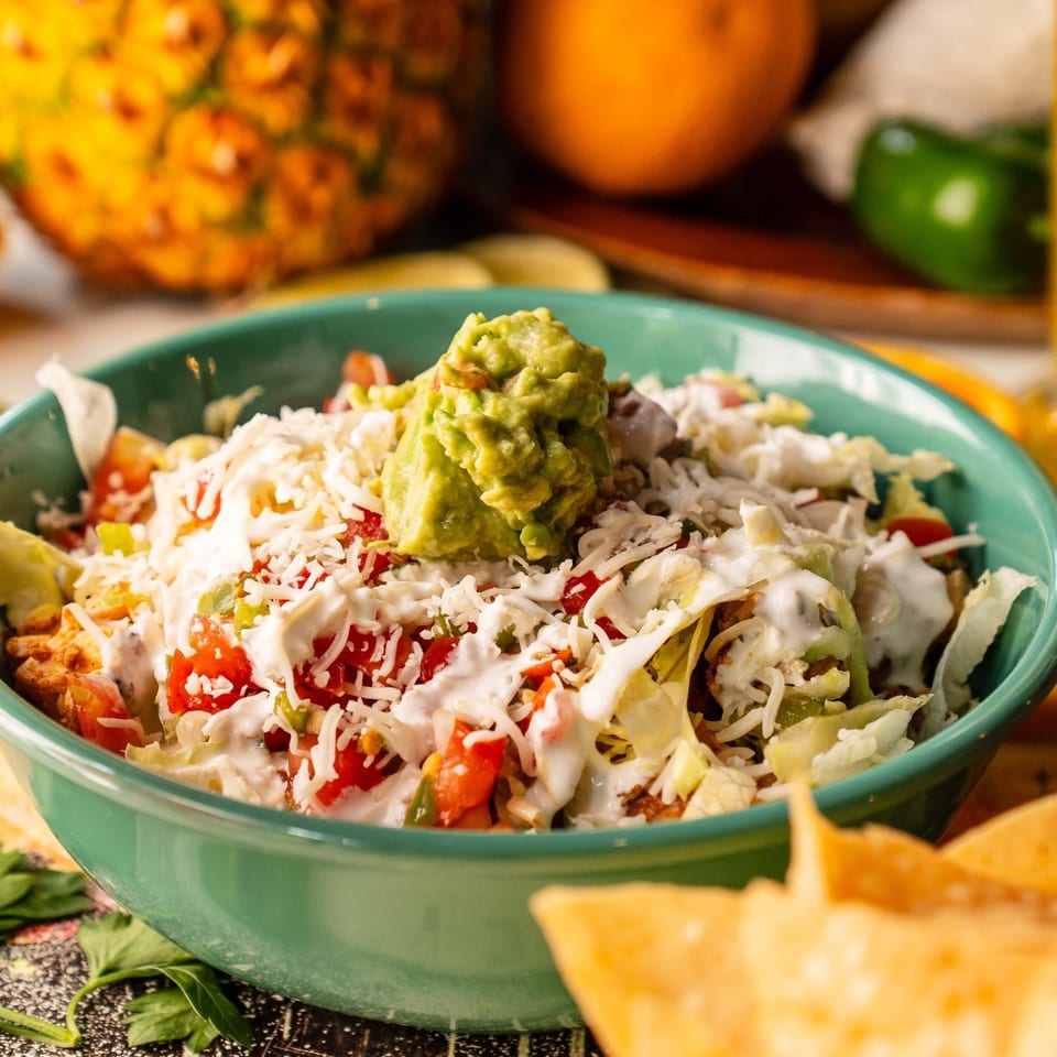 Burrito bowl topped with guacamole, shredded cheese, lettuce, and sauce.
