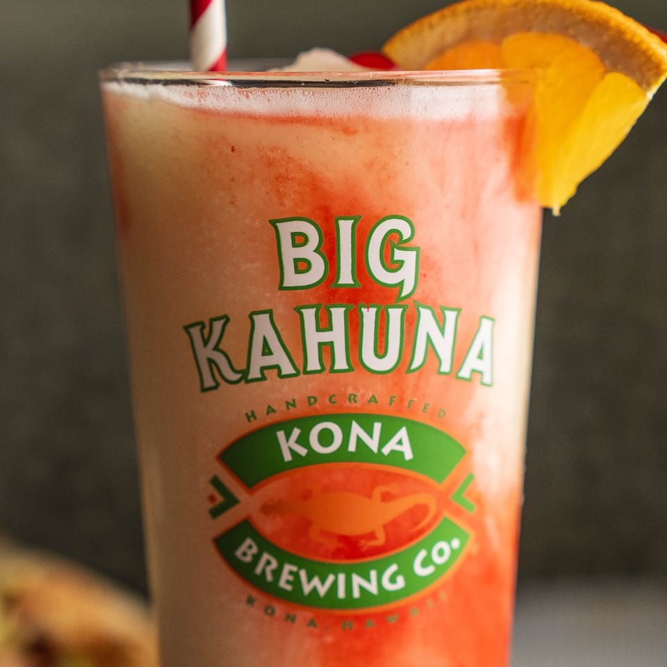 Strawberry pina colada with an orange garnish in a Big Kahuna glass.