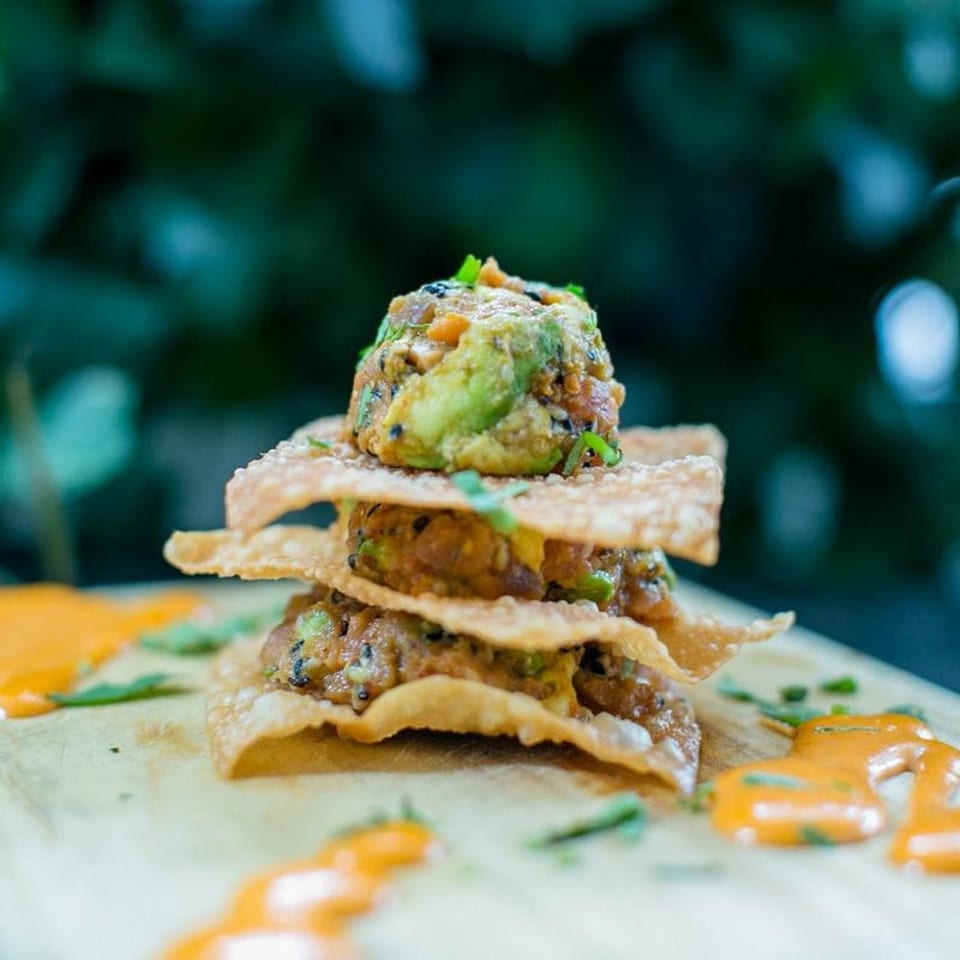 Stacked tuna and avocado tartare on crispy wonton crackers with orange sauce on a wooden board.