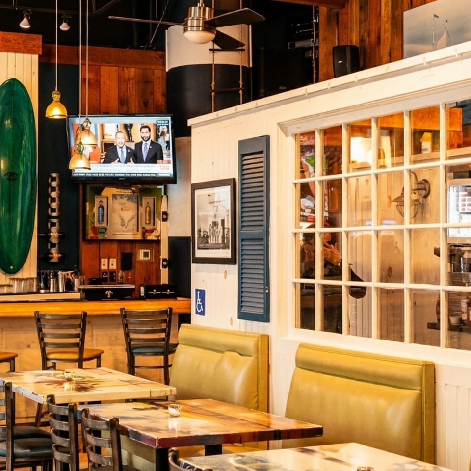 Casual restaurant interior featuring a bar, dining tables, booths, and a decorative green surfboard.