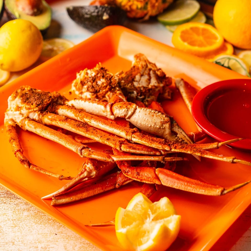 Seasoned crab legs served on an orange tray with lemon wedges and dipping sauce.
