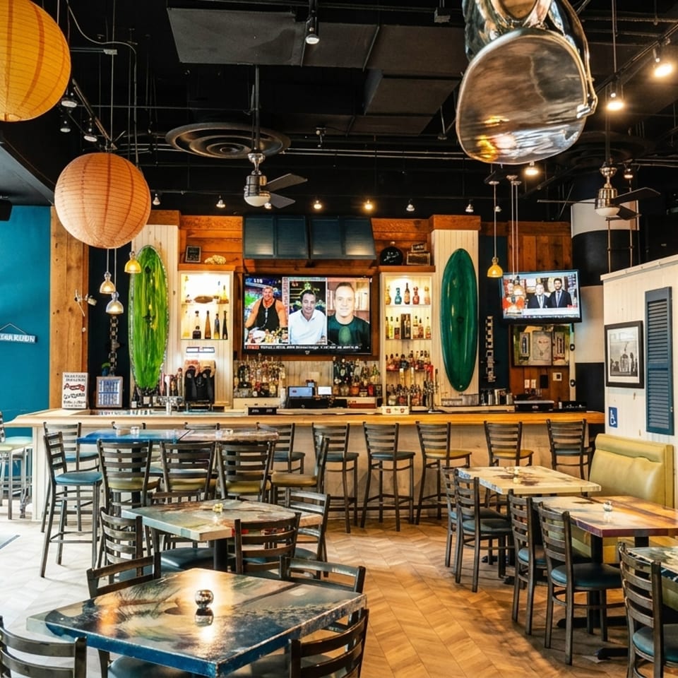 Casual restaurant interior with a full bar, dining tables, booths, and surfboard decor.