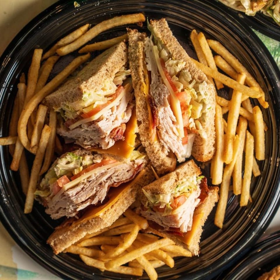 Four club sandwich halves with turkey, bacon, cheese, lettuce, and tomato, served with fries.