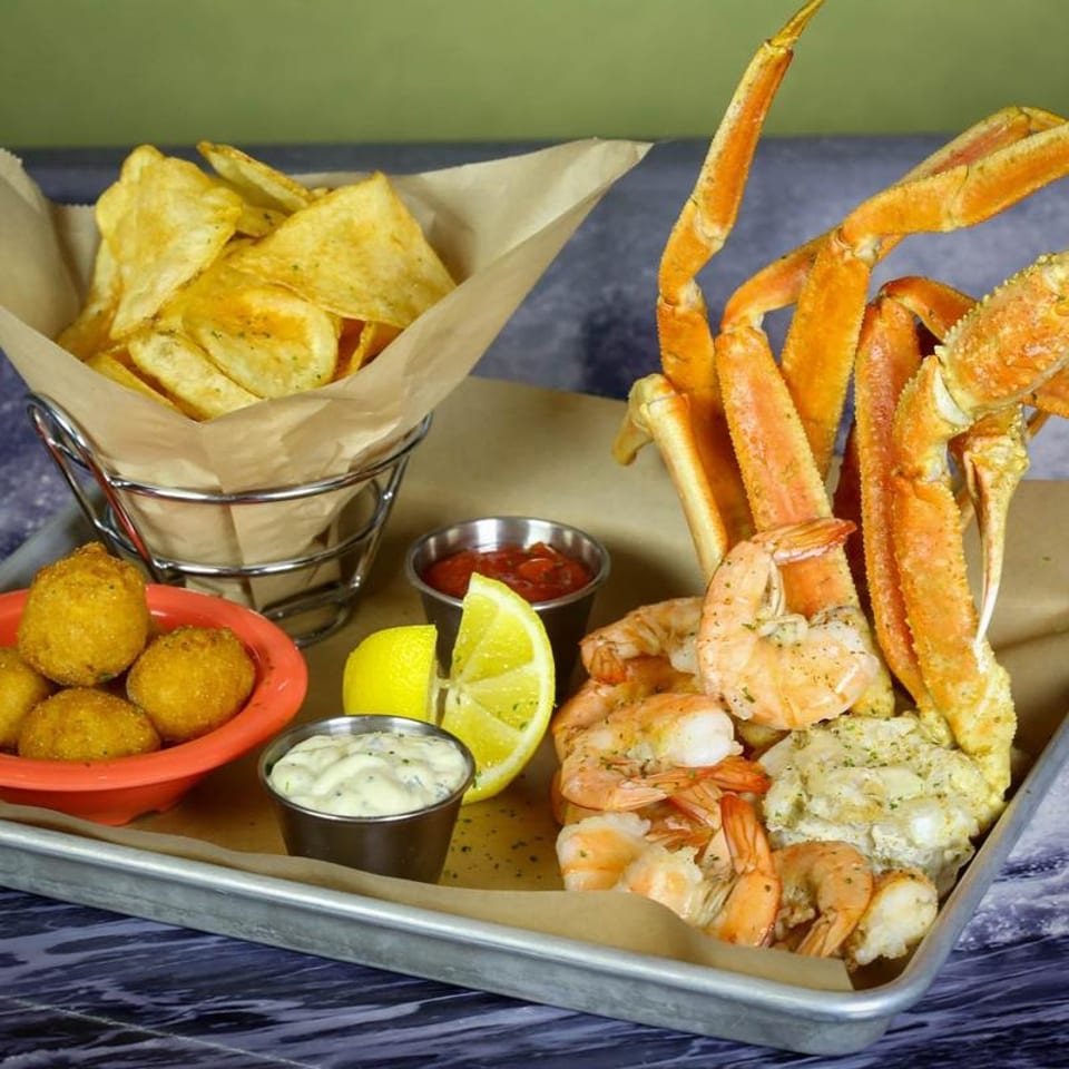 Seafood platter with crab legs, shrimp, hush puppies, chips, lemon, cocktail sauce, and tartar sauce.