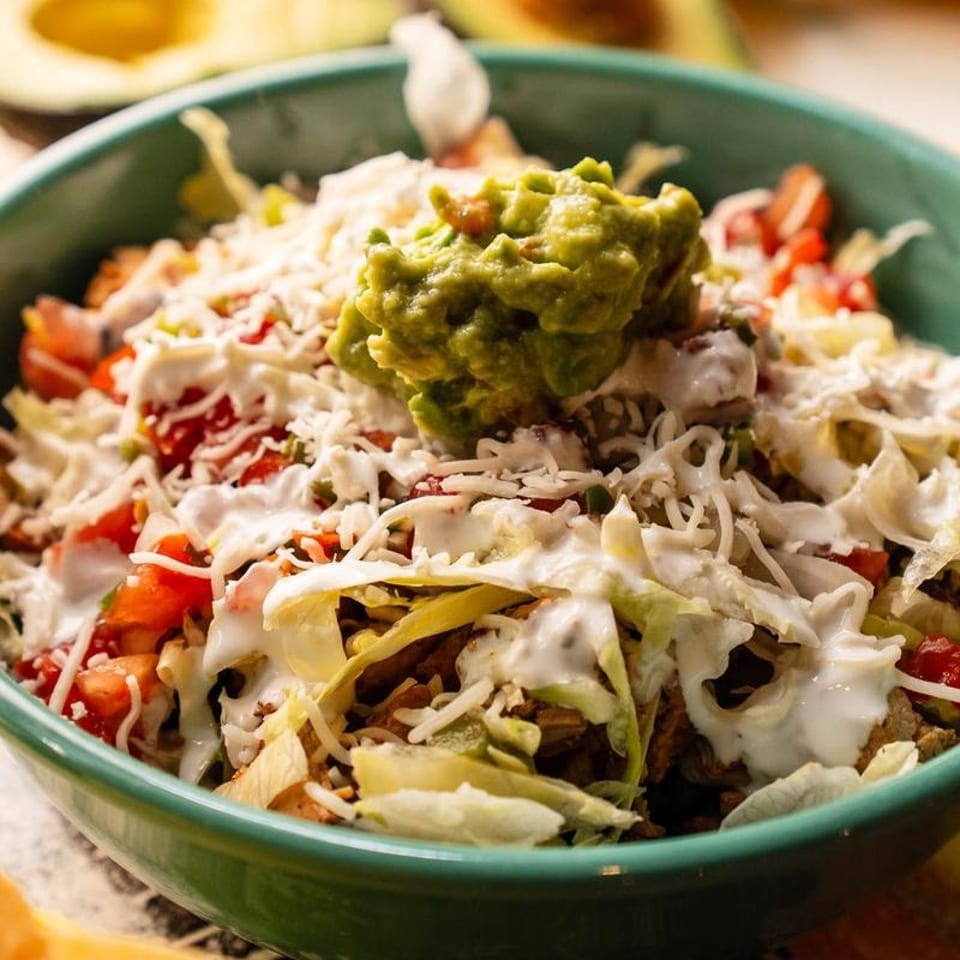 Close-up of a vibrant taco salad bowl with guacamole, cheese, lettuce, and tomatoes.