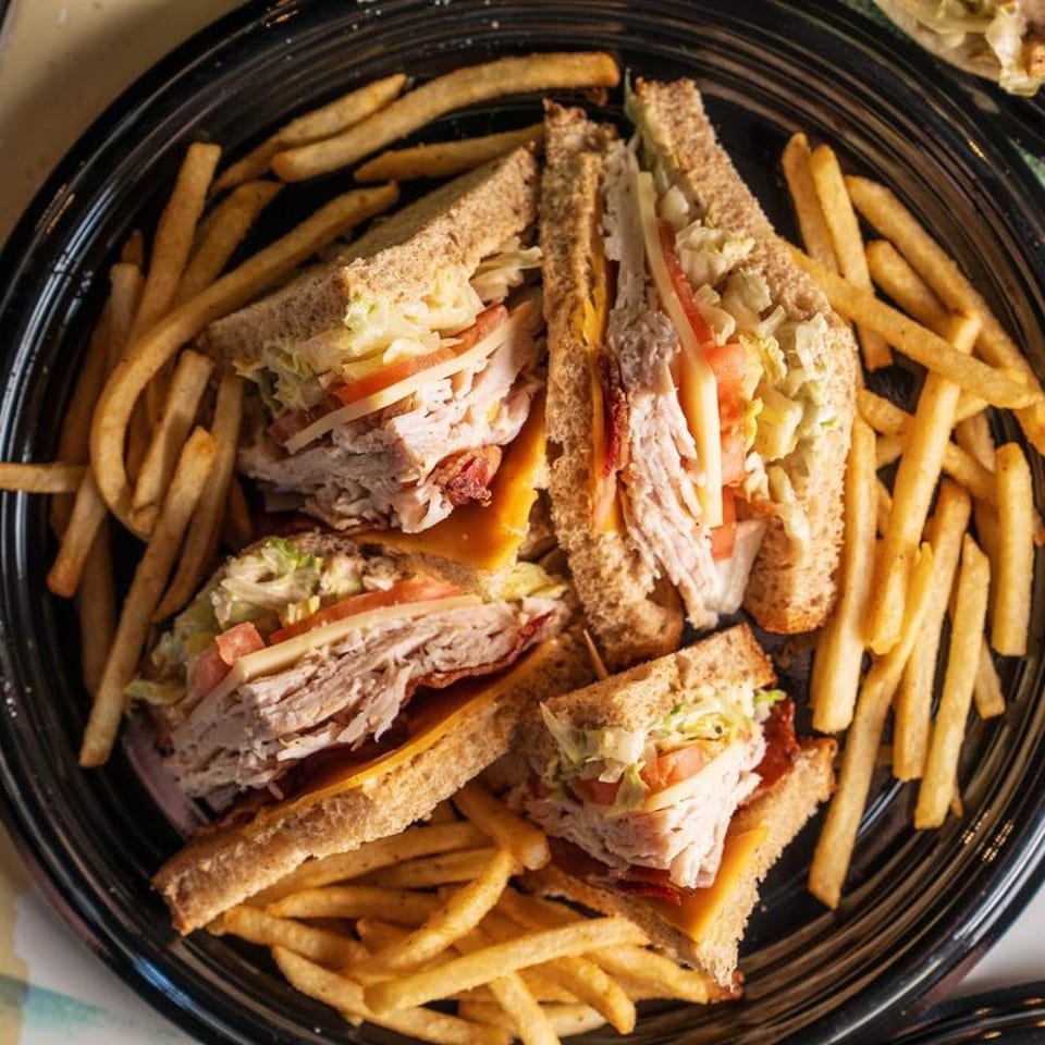 A black plate filled with golden french fries and four turkey club sandwich halves.