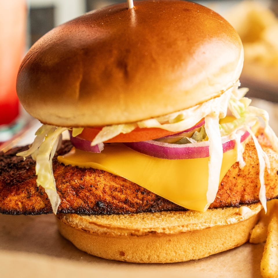 Salmon sandwich with cheese, lettuce, tomato, red onion, and fries.