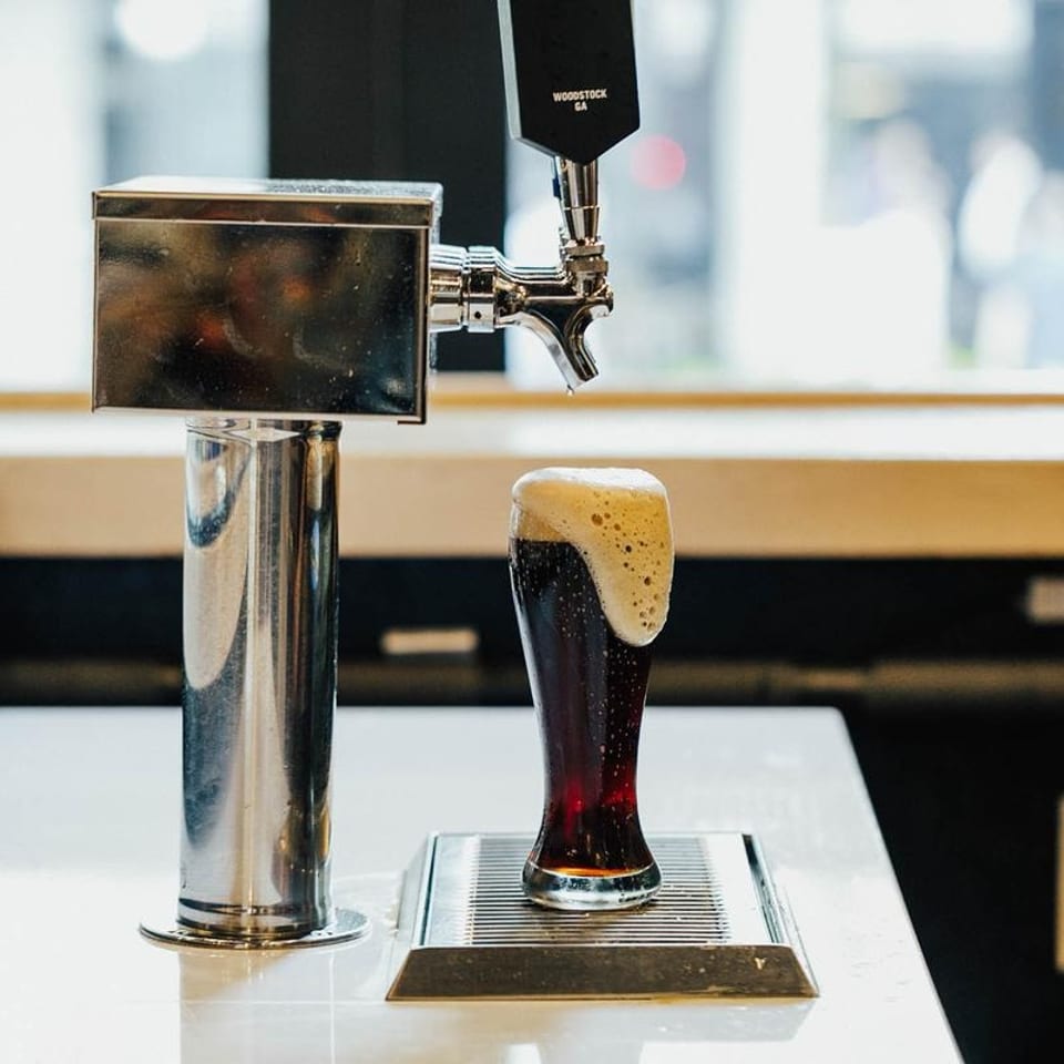 Dark beer with a foamy head overflowing from a glass next to a beer tap.