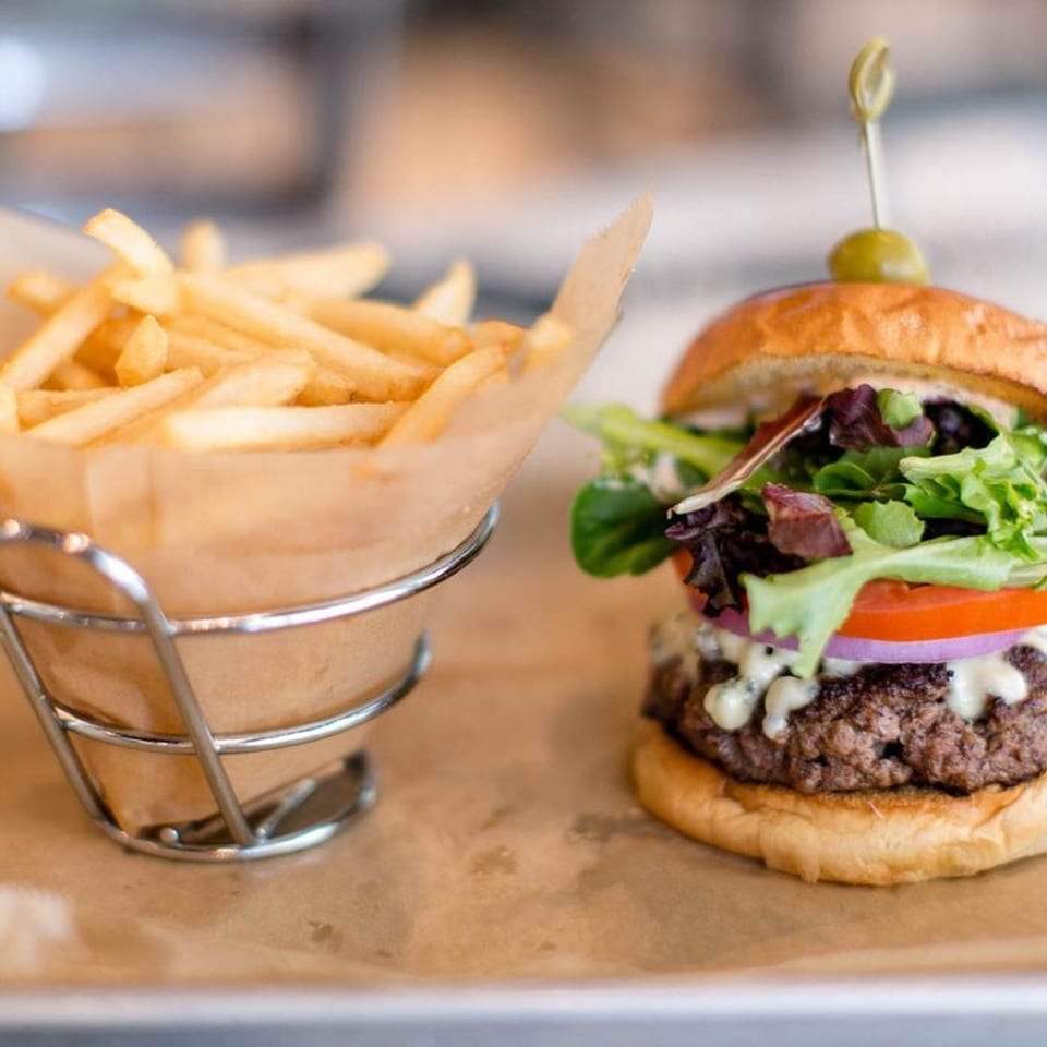 Gourmet burger with lettuce, tomato, onion, and blue cheese, served with a side of golden fries.