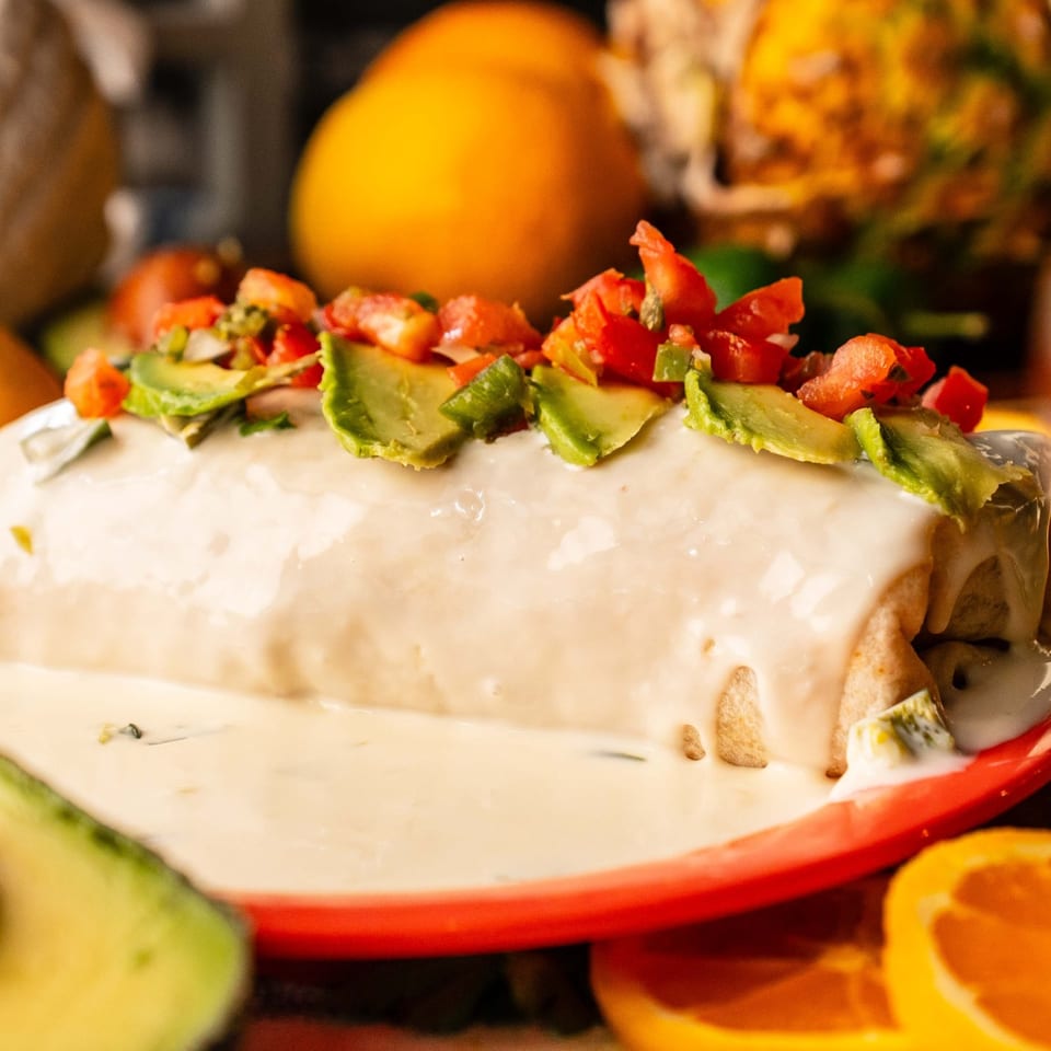 Smothered burrito topped with white sauce, avocado, and pico de gallo.