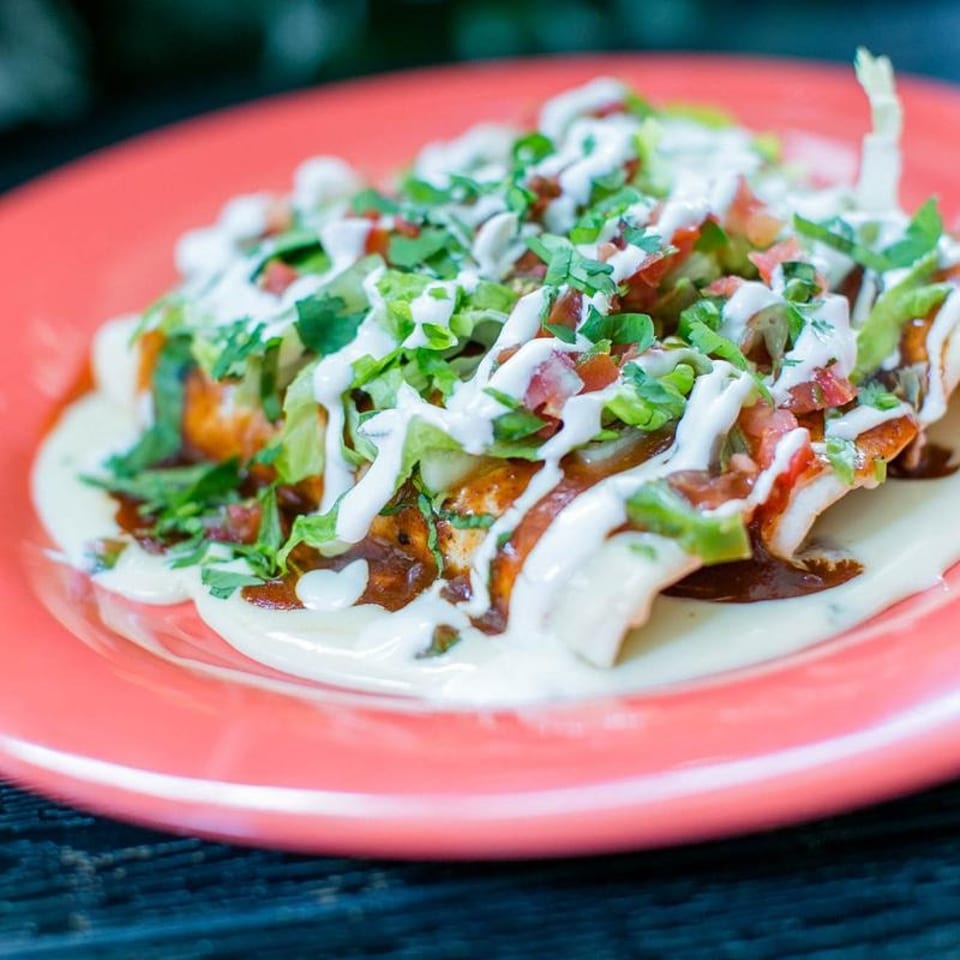 Chicken enchiladas topped with lettuce, pico de gallo, and white sauce on a red plate.