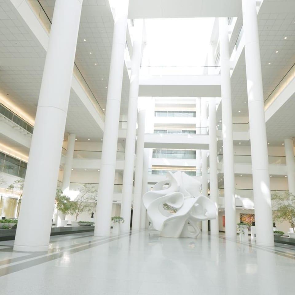 A bright, modern atrium with tall white pillars, balconies, and a large abstract white sculpture.