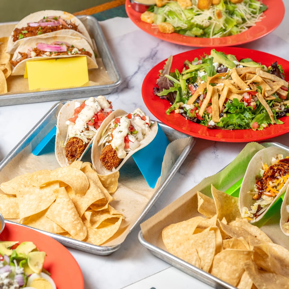 A vibrant spread of tacos and salads on a white marble table, showcasing various fresh ingredients.