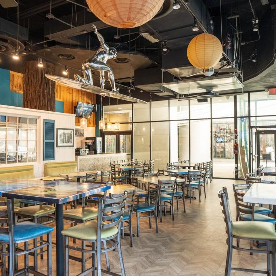 Restaurant interior with colorful tables, chairs, and a silver surfer sculpture hanging from the ceiling.