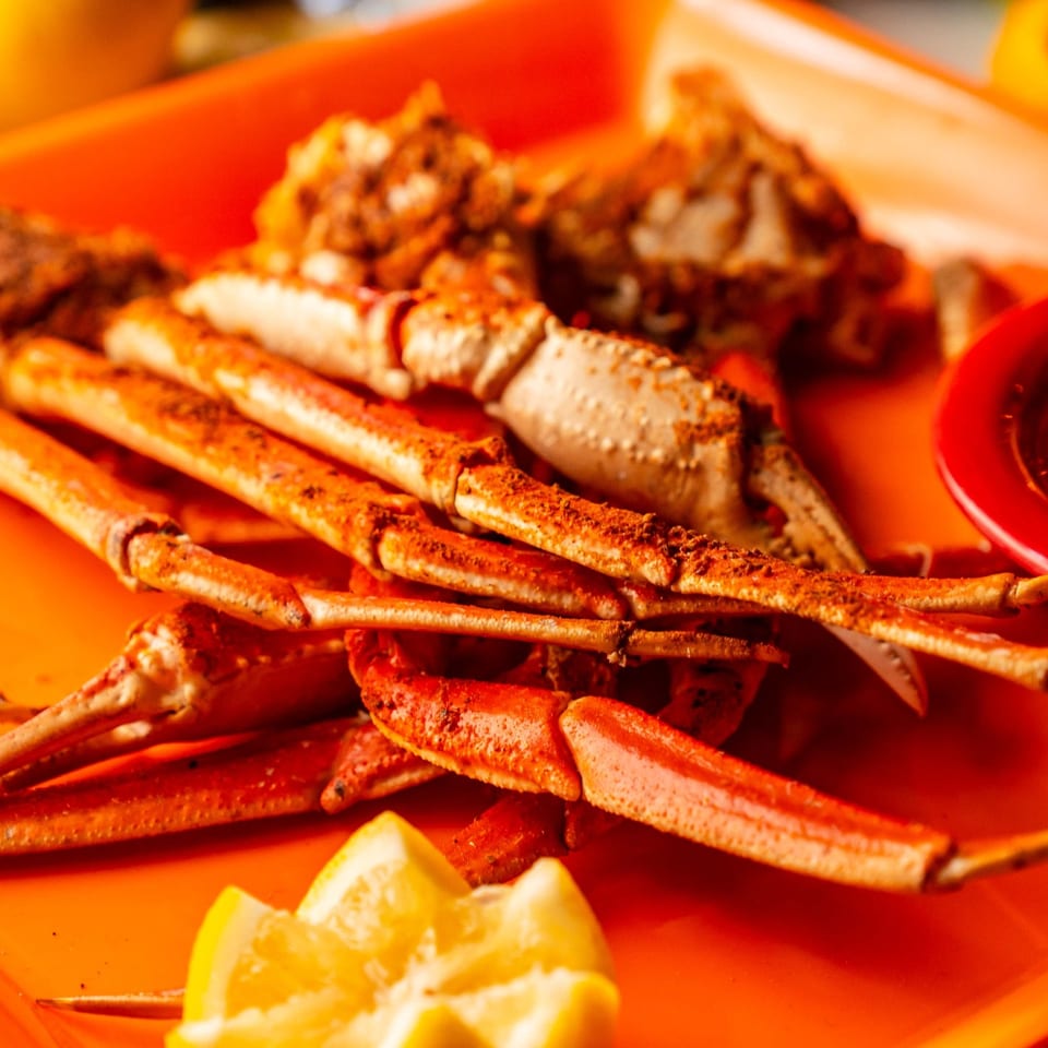 Crab legs with lemon and dipping sauce on an orange plate.