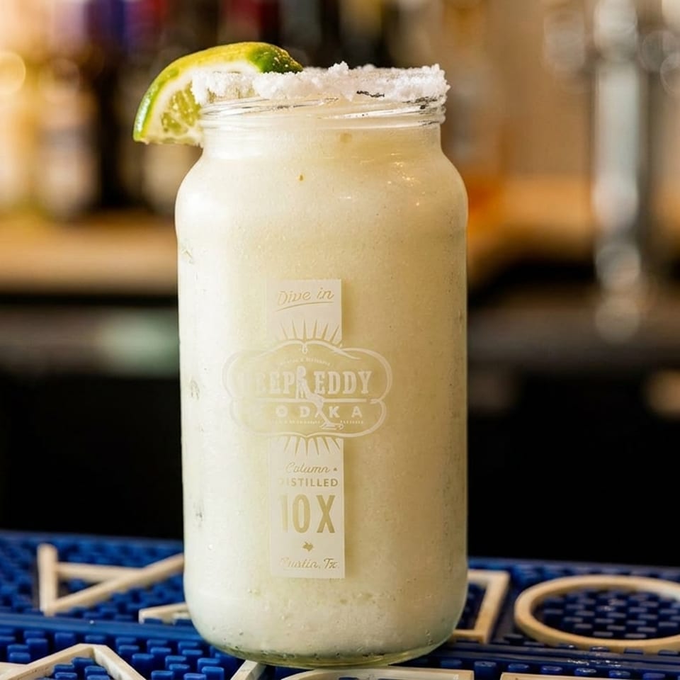 Frozen drink in a Deep Eddy Vodka mason jar with a salted rim and lime wedge on a bar mat.