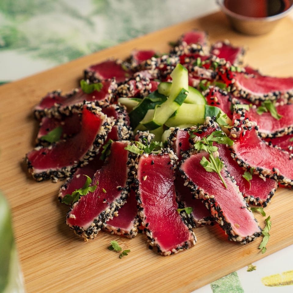 Sesame-crusted tuna slices arranged on a board with cucumber.