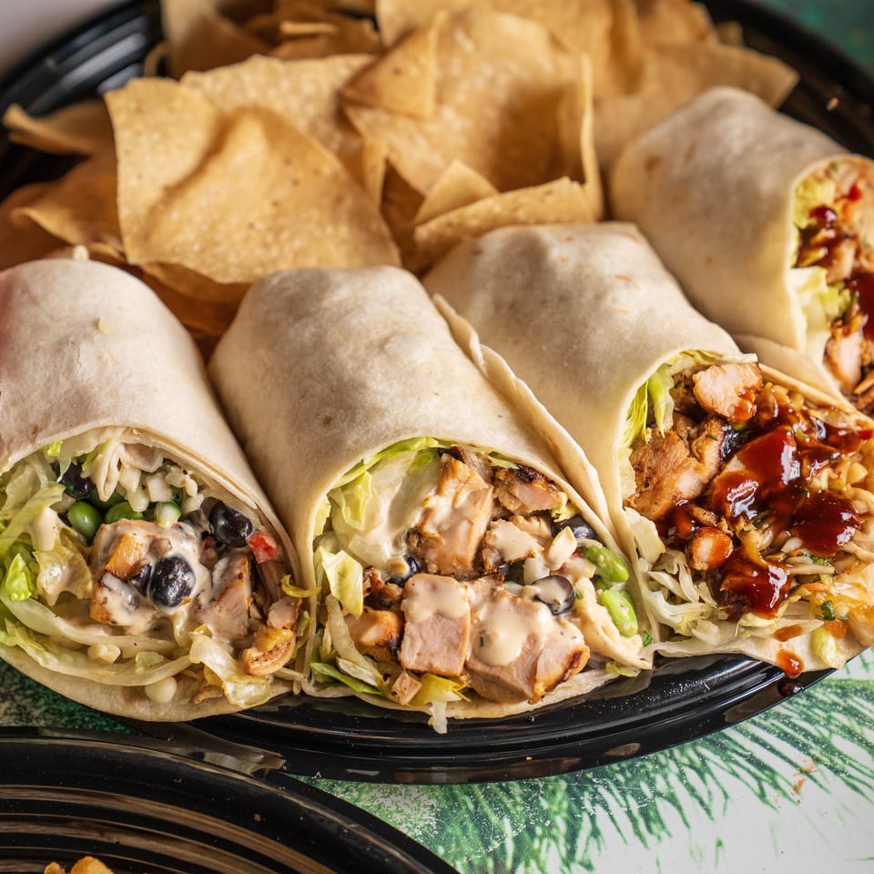 Four wraps with various fillings and sauces, served with tortilla chips on a black platter.