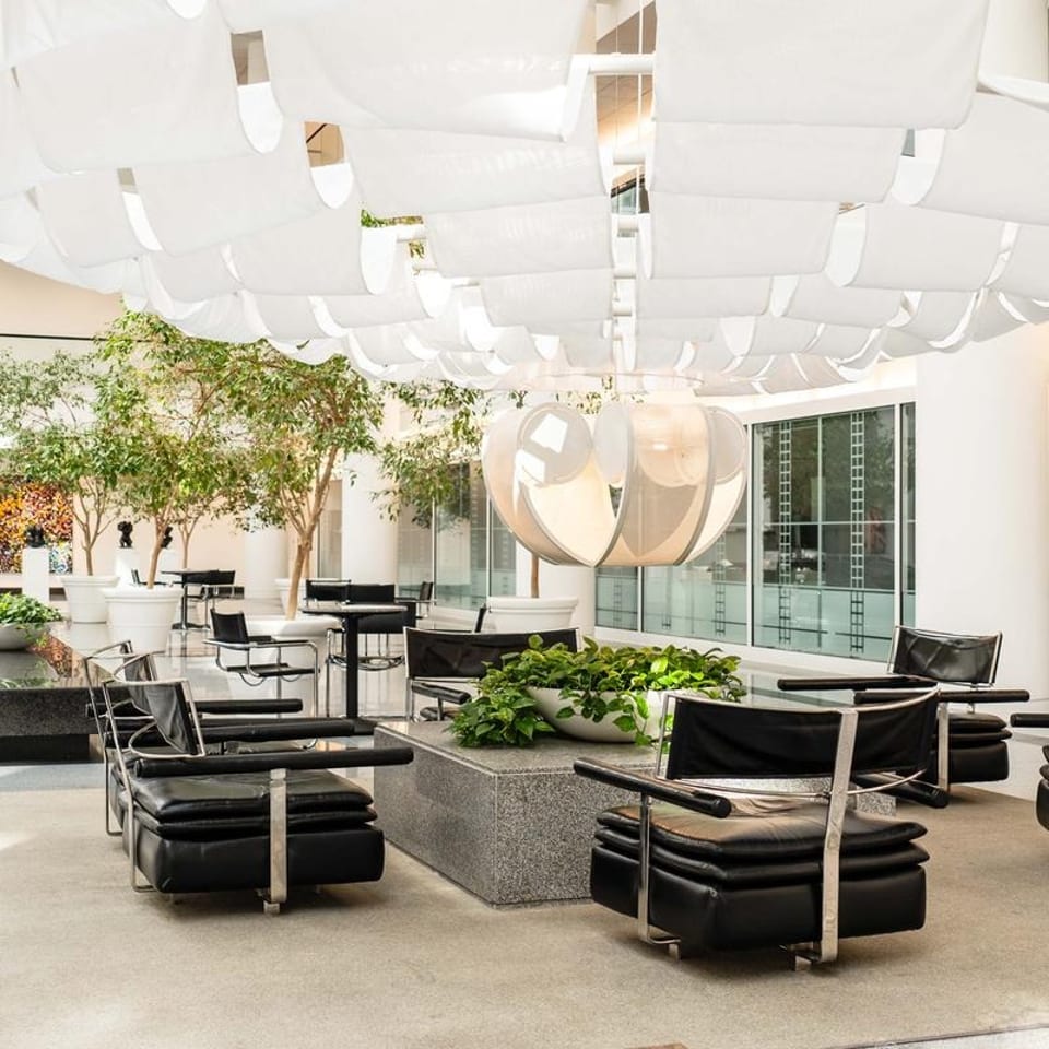 Modern lounge area with black leather chairs, potted plants, and a large white chandelier.
