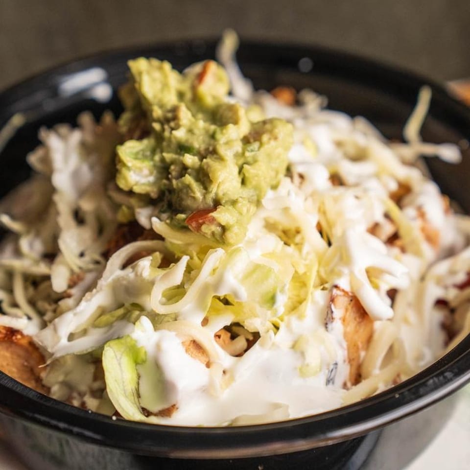 A close-up of a burrito bowl with guacamole, sour cream, cheese, and lettuce.